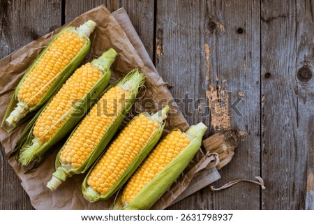 top view of cooked and uncooked corn cobs on left side and wooden background with copy space