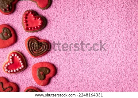 Top view of cookies in shape of hearts decorated by pink icing, chocolate and sprinkles on light-pink background