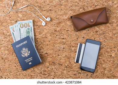 Top view of cork table with blank smartphone, credit car, american passport and dollars, eyeglass case and headphones. Traveling concept. Mock up