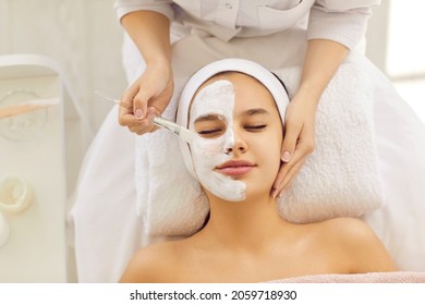 Top view of cosmetologist do facial mask for healthy glowing skin for smiling female client. Dermatologist make beauty procedures for woman patient in aesthetic medical clinic. Cosmetology concept.