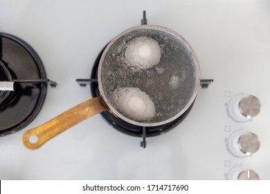 Top View Couple Of Eggs Boiling In A Pot With Full Of Water With White Oven Background.