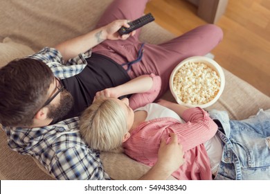 Top view of a couple enjoying their leisure time, watching television and eating popcorn. Selective focus