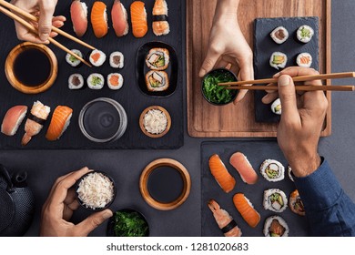 Top view of couple hands eating sushi food at japanese restaurant. High angle view of woman hand serving seaweed in to man. Couple eating and sharing sushi roll, maki, nigiri, uramaki.