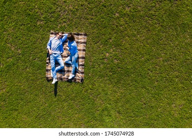 Top View Of Couple Lying On A Picnic Blanket On The Grass.