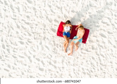 Top View Of Couple Lying On White Sand Beach Taking A Sunbath In Summer 