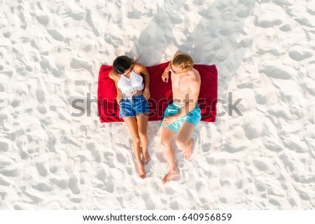 Top view of couple lying on white sand beach taking a sunbath in summer