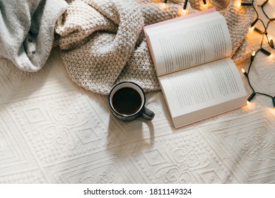 Top view of cozy blanket, open book and hot cup of coffee on bed on a cold winter day. Relaxation and hygge concept. Top view with copy space