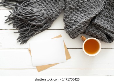 Top View Cozy Home Desk With Knitted Plaid, Tea Cup, Letter, Blank Paper Card On Wooden White Background. Flat Lay, Top View. Nordic, Hygge, Comfort Concept