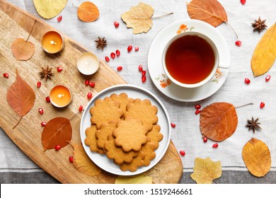 Top view of a cozy homemade tea party.  Autumn composition. Cup of hot tea, Gingerbread cookie, burning candles, yellow fallen leaves, seeds pomegranate, anise on a linen tablecloth. Flat lay - Powered by Shutterstock