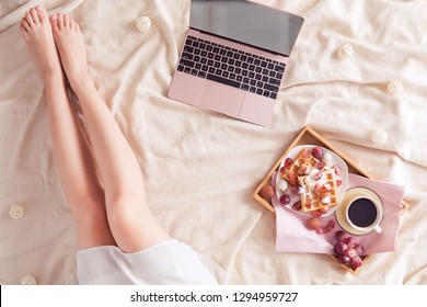 Top view of cozy workspace with woman legs, pink air laptop, coffee cup, waffles with fruit. Flat lay, top view - Powered by Shutterstock