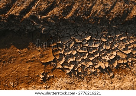 Top view of cracked mud and dry earth revealing drought-stressed riverbed textures at sunset, directly above