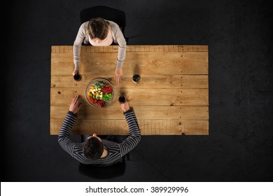 Top view creative photo of couple sitting at wooden vintage table. Man and woman having romantic dinner. They with cheese plate and glasses with wine