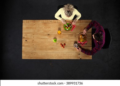 Top view creative photo of couple sitting at wooden vintage table. Man and woman having romantic dinner. They with plates full of delicious meal and glasses with wine