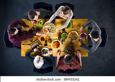 Top view creative photo of friends sitting at wooden vintage table. Friends of six having dinner. They with plates full of delicious meal and glasses with drinks