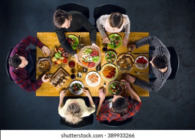 Top view creative photo of friends sitting at wooden vintage table. Friends of six having dinner. They with plates full of delicious meal and glasses with drinks