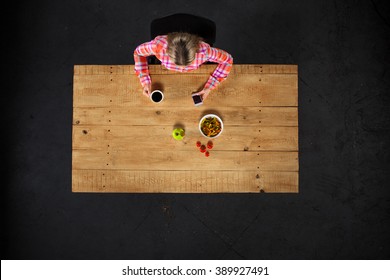 Top View Creative Photo Of Girl Sitting At Wooden Vintage Table. Girl With Plate Full Of Delicious Meal. Girl Using Mobile Phone