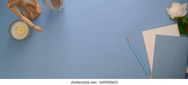 Top view of creative workspace with diary notebooks, decorations and copy space on light blue table 