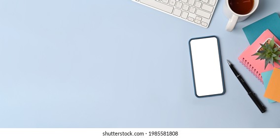 Top view creative workspace with smart phone, sticky note, coffee cup and notebook on blue background.