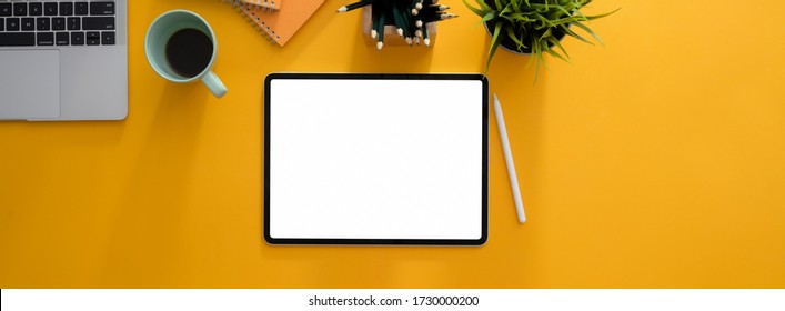 Top view of creative worktable with blank screen tablet, stationery, coffee mug and decoration on yellow desk 