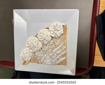 Top view of a crepe served with generous dollops of whipped cream and sprinkled with powdered sugar on a square white plate. A delicious sweet treat for dessert or breakfast. - Powered by Shutterstock