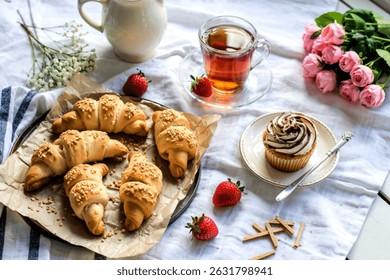 top view of crescent roll crunchy crispbread on cloth and cup of tea with strawberries and cupcake