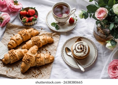 top view of crescent roll crunchy crispbread on cloth and cup of tea with strawberries and cupcake