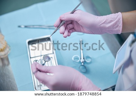 Top view cropped head close up of woman hands in latex gloves holding dental mirror and explorer