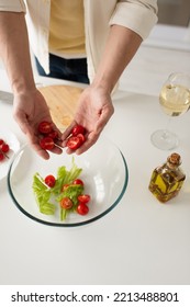 Top View Of Cropped Man Holding Cut Cherry Tomatoes Near Bowl With Salad And Bottle Of Oil