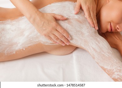 Top View Cropped Shot Of A Sexy Woman Smiling, Getting Body Wrap Treatment At Spa. Spa Therapist Applying Body Mud Mask On The Back Of A Female Client