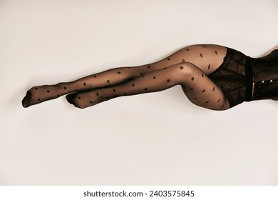 top view of cropped young woman in black corset and polka dot tights lying on white floor