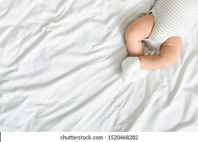 Top View Of Crossed Legs Of Newborn Baby Lying On Bed In Bodysuit And Socks, Panorama With Free Space