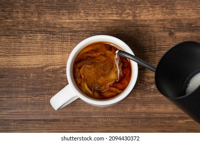 Top View Of A Cup Of Black Coffee Mix Ing With Milk