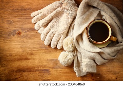 Top view of Cup of black coffee with a warm scarf and gloves on wooden background. filreted image 
