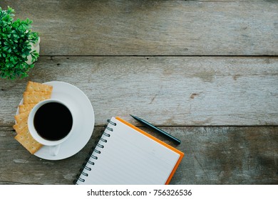 Top view of cup of coffee, cracker, notepad on wooden table