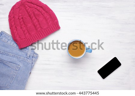 Top view of a cup of coffee and a woman's outfit on a white wooden table. Cozy atmosphere concept. Winter and autumn season.