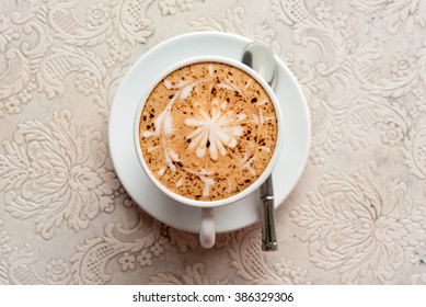 Top View Of A Cup Of Hot Cappuccino Coffee On Beautiful Patterned Table Runner.