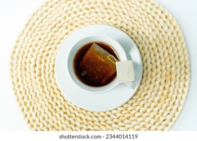 A top view of a cup of tea placed on a round woven coaster, alongside an herbal tea bag and a product labels without a logo on the rim. All objects are centered in the image. - Powered by Shutterstock