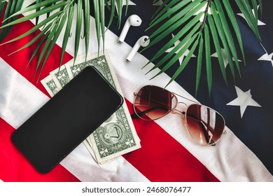 Top view of currency us dollar, sunglasses, smartphone, and palm leaf on usa flag, suggesting preparation for journey. Travel essentials on us surface. Travel vacation concept. Copy ad text space - Powered by Shutterstock