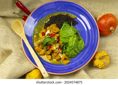 A Top View Of Curry With Mango Chicken And Black Lentils On A Blue Plate With A Wooden Spoon