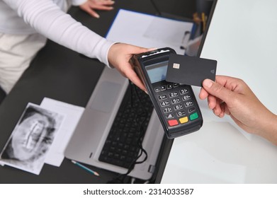 Top view customer hand holding a black mockup credit card above a POS terminal, making wireless or cashless payment using NFC technology. Close-up. Copy advertising space. People, business and finance