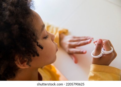 Top View Of A Cute Little Mixed Race Girl Making Manicure Cutting Nails With Scissors Indoors.	Copy Space.