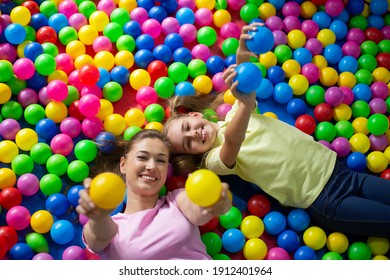 Top View Of Cute Teenage Girl With Her Mother Lying In Ball Pond At Entertainment Centre. Overhead Shot Of Parent And Teen Child Playing Together, Having Fun At Kids Playground. Family Pastimes