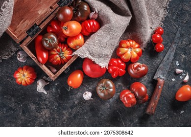 Top view of dark table surface with colorful homemade organic tomatoes, garlic, wooden box and vintage knife. Homemade vegetables harvest concept.