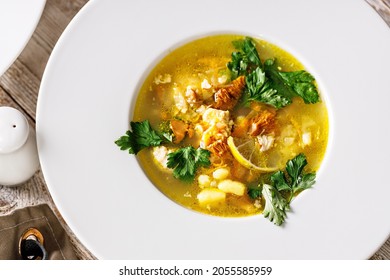 Top View Delicious Autumn Soup With Chanterelles And Fresh Herbs. Seasonal Dish With Edible Mushrooms. White Plate And Cutlery On A Rustic Background. Food Still Life. Vegetarian Dinner