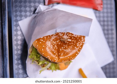 Top view of a delicious burger with sesame seed bun, fresh lettuce and tomato wrapped in paper, Closep of hamburger on the tray on the table  in fast food restaurant; - Powered by Shutterstock