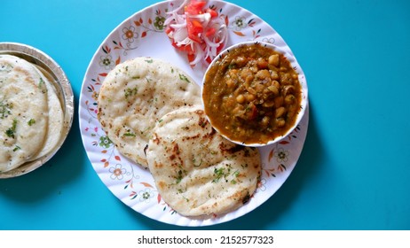 Top View Of Delicious Chole Kulcha Served In A White Designer Plate With Some Salad And Extra Kulchas Byside On A Blue Background