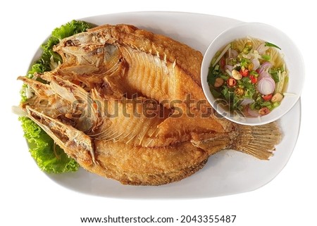 Top view of delicious deep fried 
Seabass fish with fish sauce served with spicy dipping sauce on white plate isolated on white background. Famous fried fish dish in Thai restaurant.