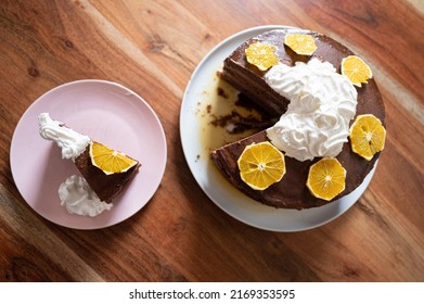 Top View Of Delicious Homemade Vegan Orange Cake Served On A Plate Next To A Whole Dessert On Domestic Dinning Table.