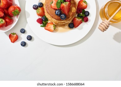 top view of delicious pancakes with honey, blueberries and strawberries on plate on marble white surface - Shutterstock ID 1586688064