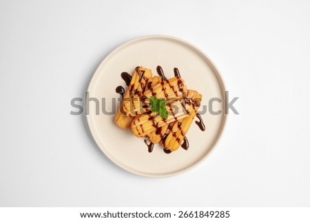 Top View of Delicious stack of golden churros drizzled with chocolate sauce and garnished with mint leaves, served on a white plate over a clean white background.